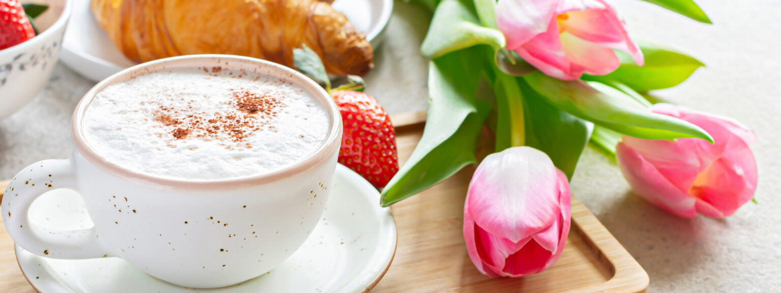 Coffee in ceramic cup on a tray with tulips and strawberries next to it.